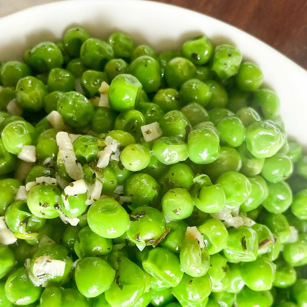 Close-up of frozen peas in garlic butter in a white bowl, glossy and fragrant.