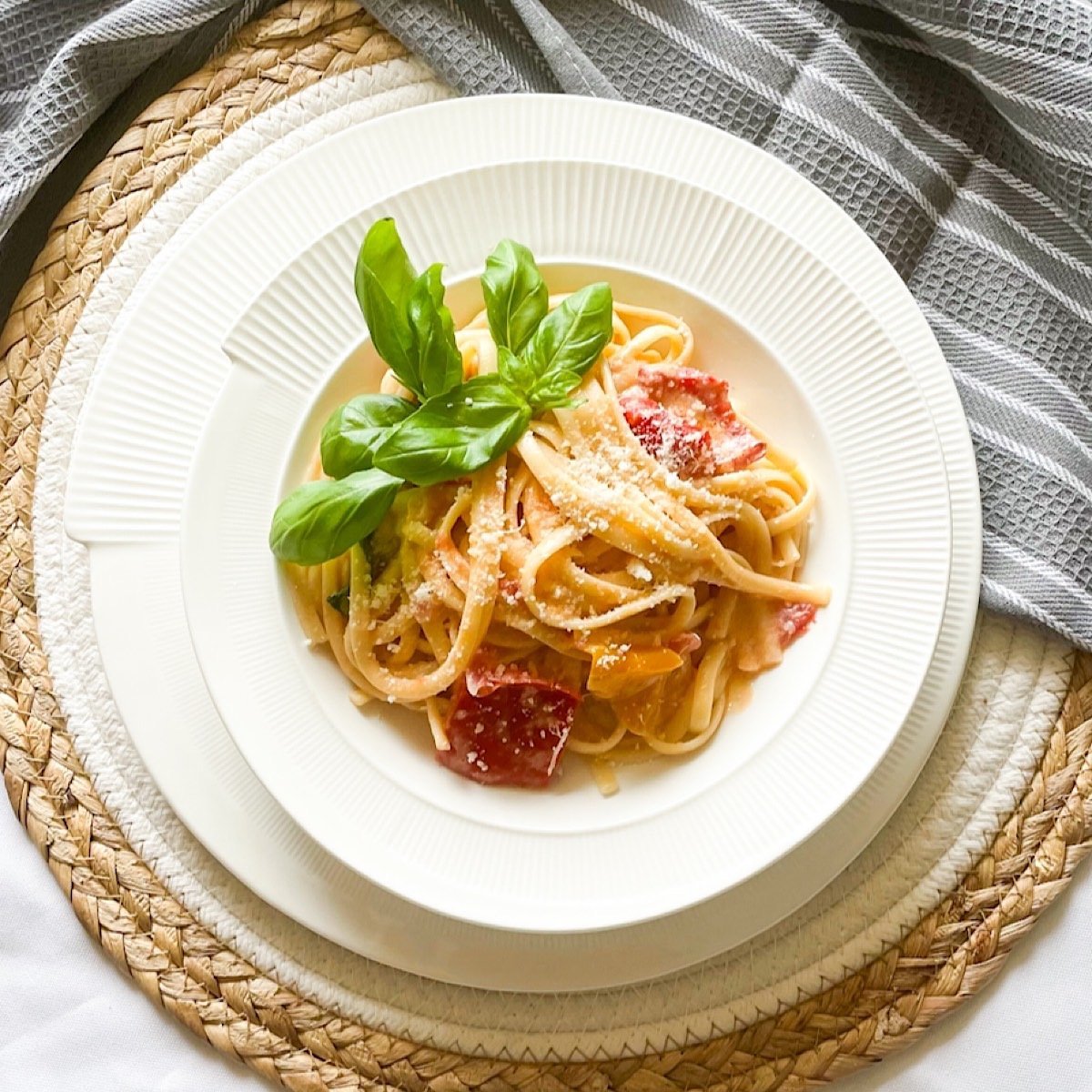 Overhead bowl of creamy roasted pepper pasta with chunks of roasted pepper, parmesan and a basil sprig