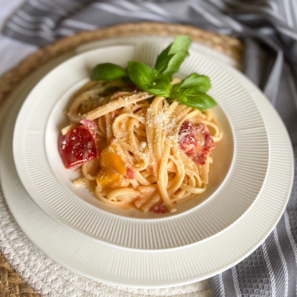 Easy roasted pepper pasta served on stacked white plates with basil and parmesan on a rustic woven mat