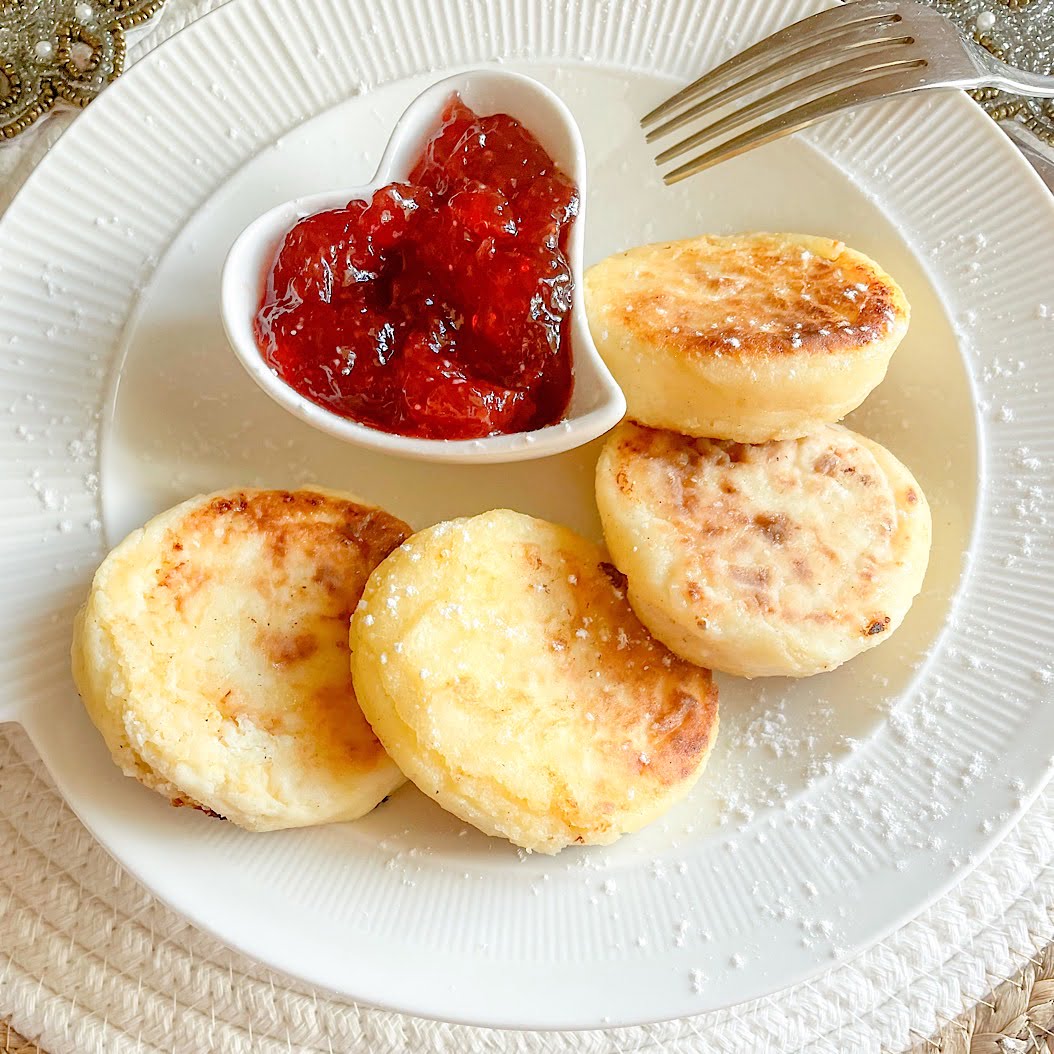 Easy Ricotta Syrniki Recipe plated with powdered sugar and a side of red berry jam.