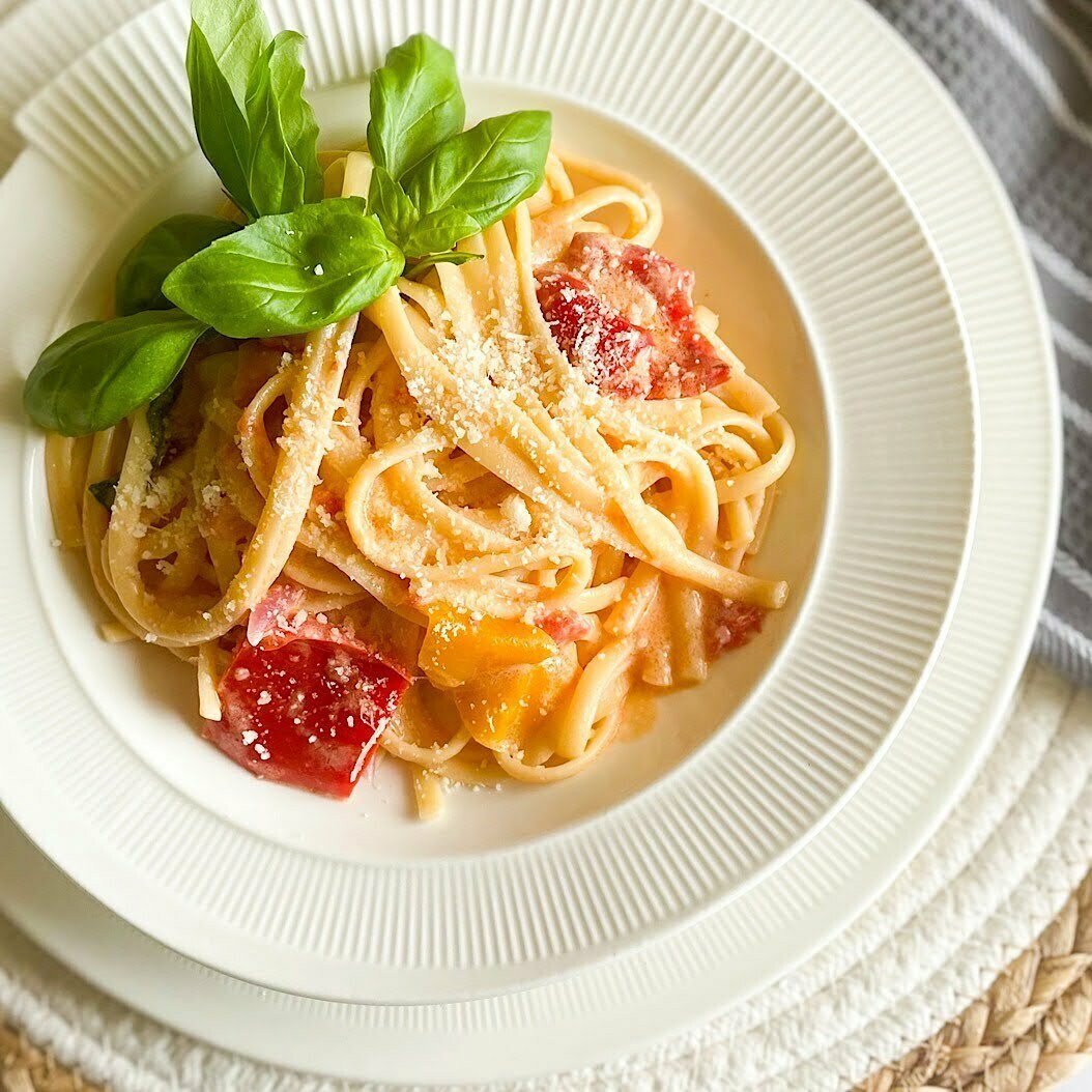 Roasted red pepper pasta piled high in a white bowl, garnished with basil and grated parmesan