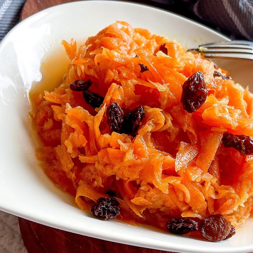 Close-up of carrot apple and raisin salad served in a white bowl on a wooden board