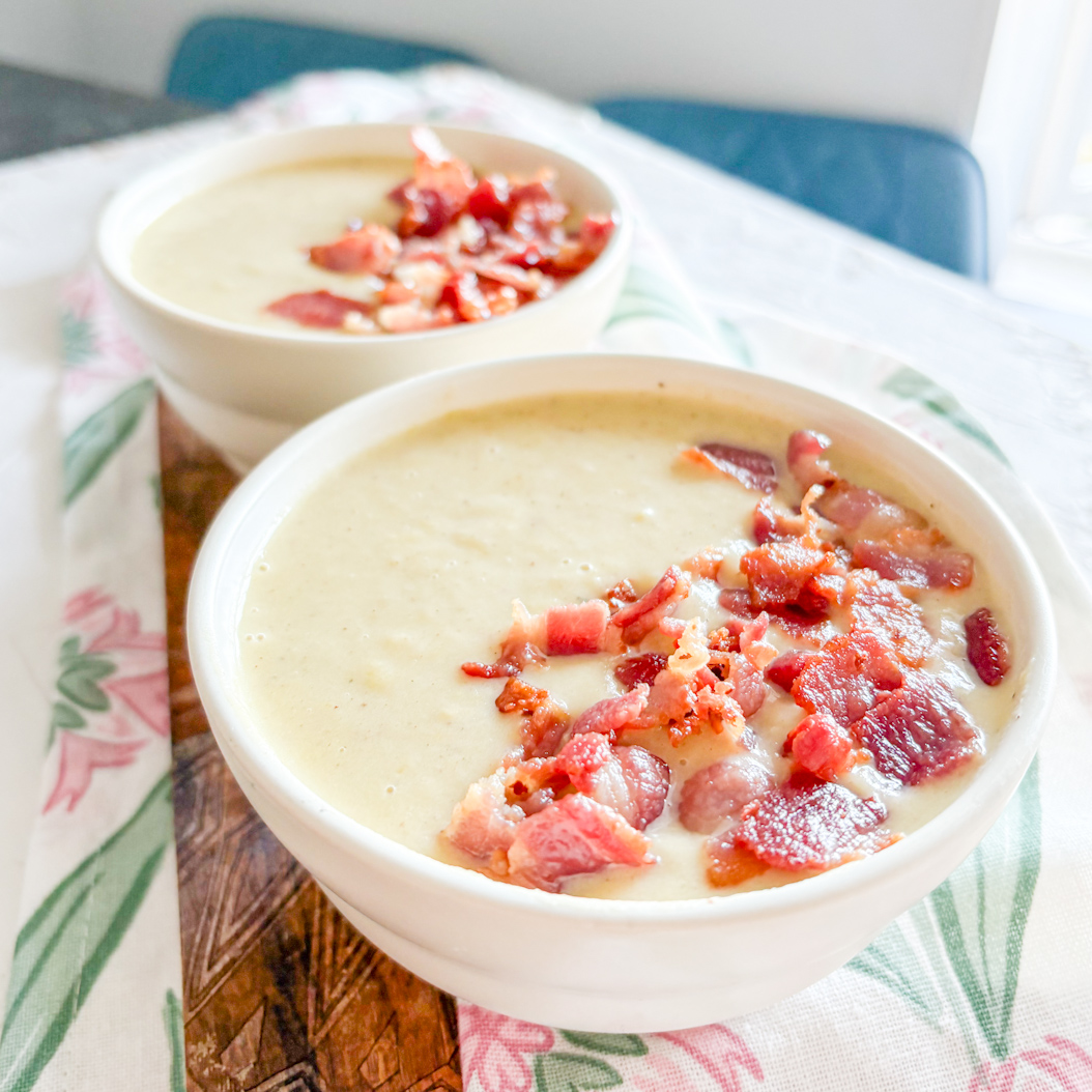 Two bowls of Leek and Potato Soup garnished with bacon, set on a floral tablecloth for a cosy presentation.