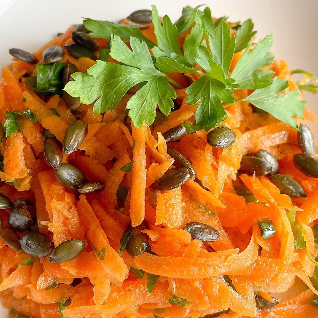 Close-up of carrot and parsley salad with shredded carrots, parsley, and pumpkin seeds.