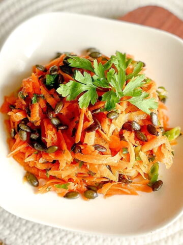 Carrot and parsley salad with toasted pumpkin seeds and fresh parsley in a white bowl.