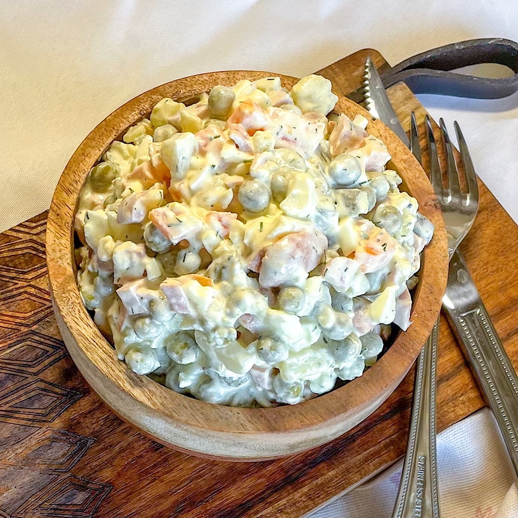 Top-down view of Russian Olivier salad with frankfurters in a wooden bowl
