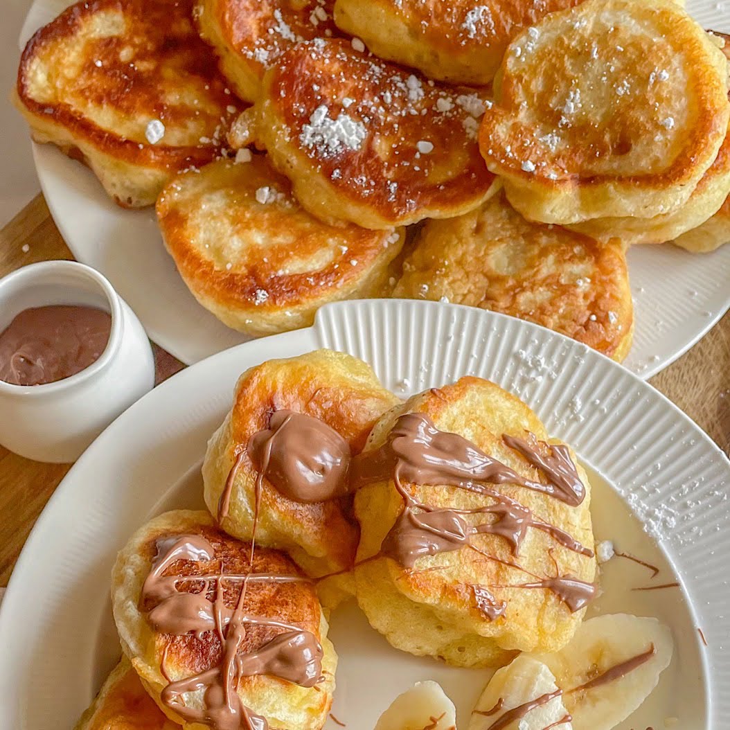 Fluffy oladi pancakes drizzled with melted chocolate and served with banana and a dusting of icing sugar