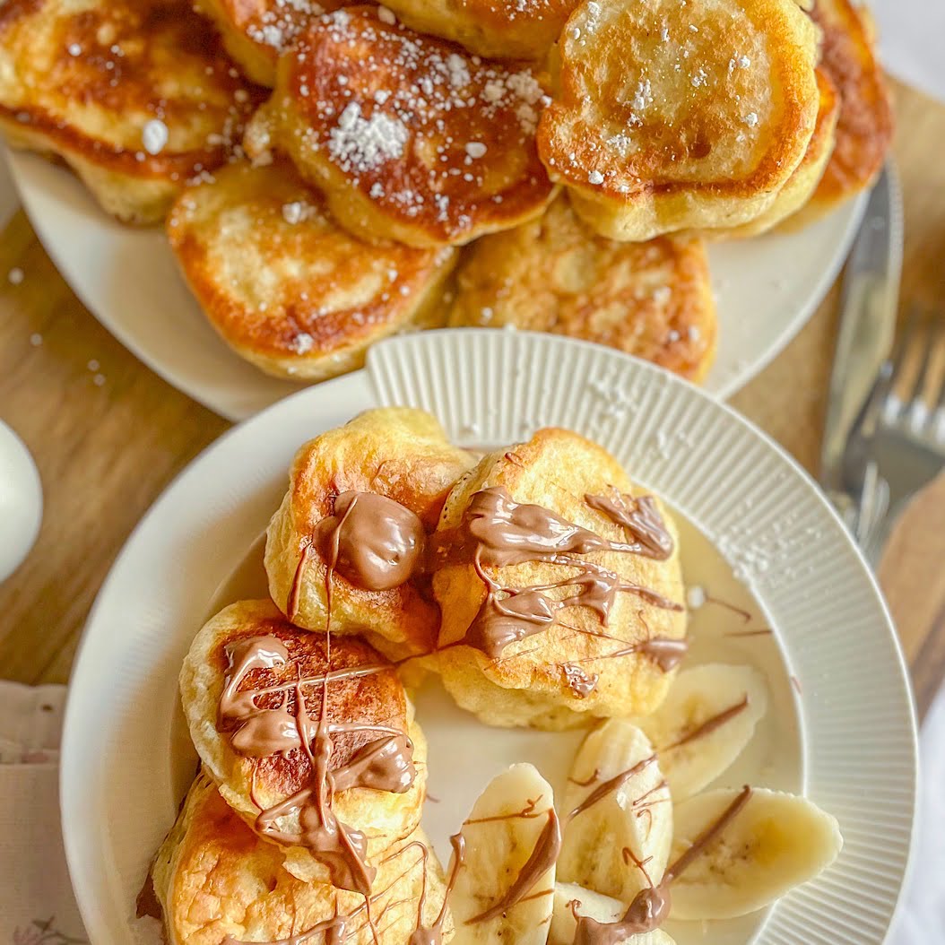 Top-down shot of homemade oladi pancakes plated with banana slices and a small jug of chocolate