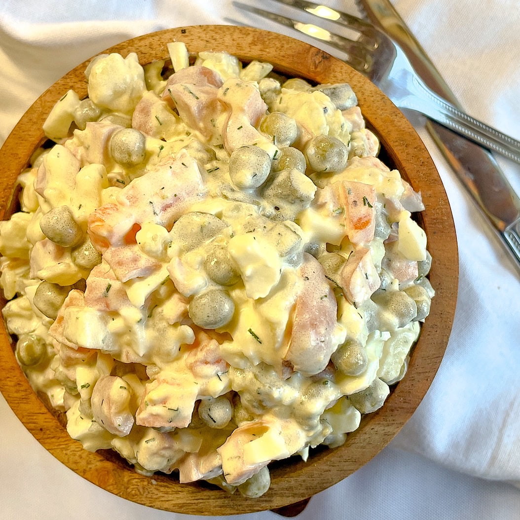 Russian Olivier salad with frankfurters ready to serve with cutlery on the side