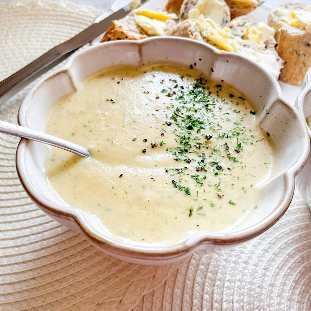 Creamy vegetable soup garnished with parsley and cracked pepper in a flower-shaped bowl, buttered bread on the side