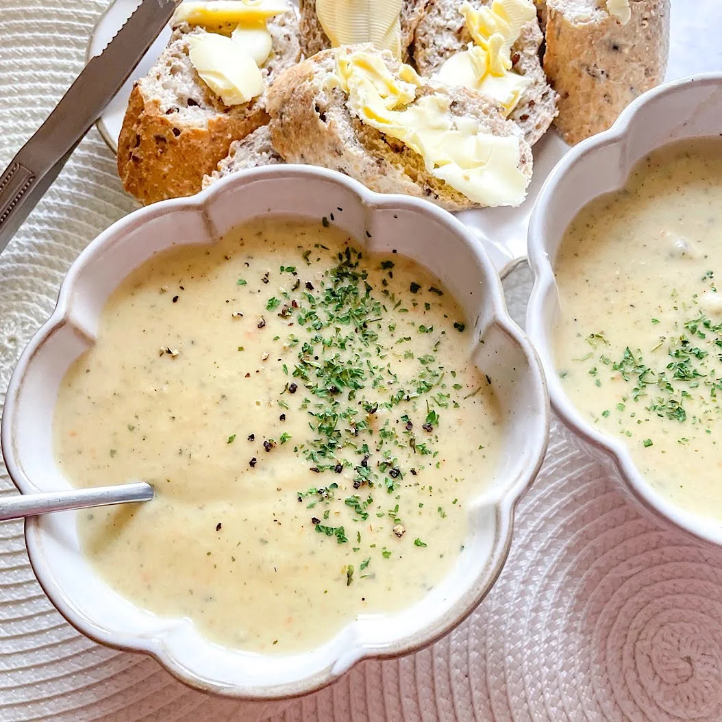 Two bowls of creamy vegetable soup with parsley garnish, served with buttered wholegrain bread