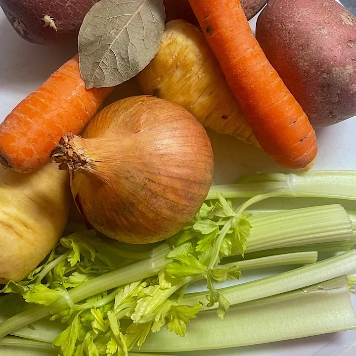 Creamy vegetable soup ingredients including potatoes, carrots, onion, parsnips, celery and a bay leaf on a white surface