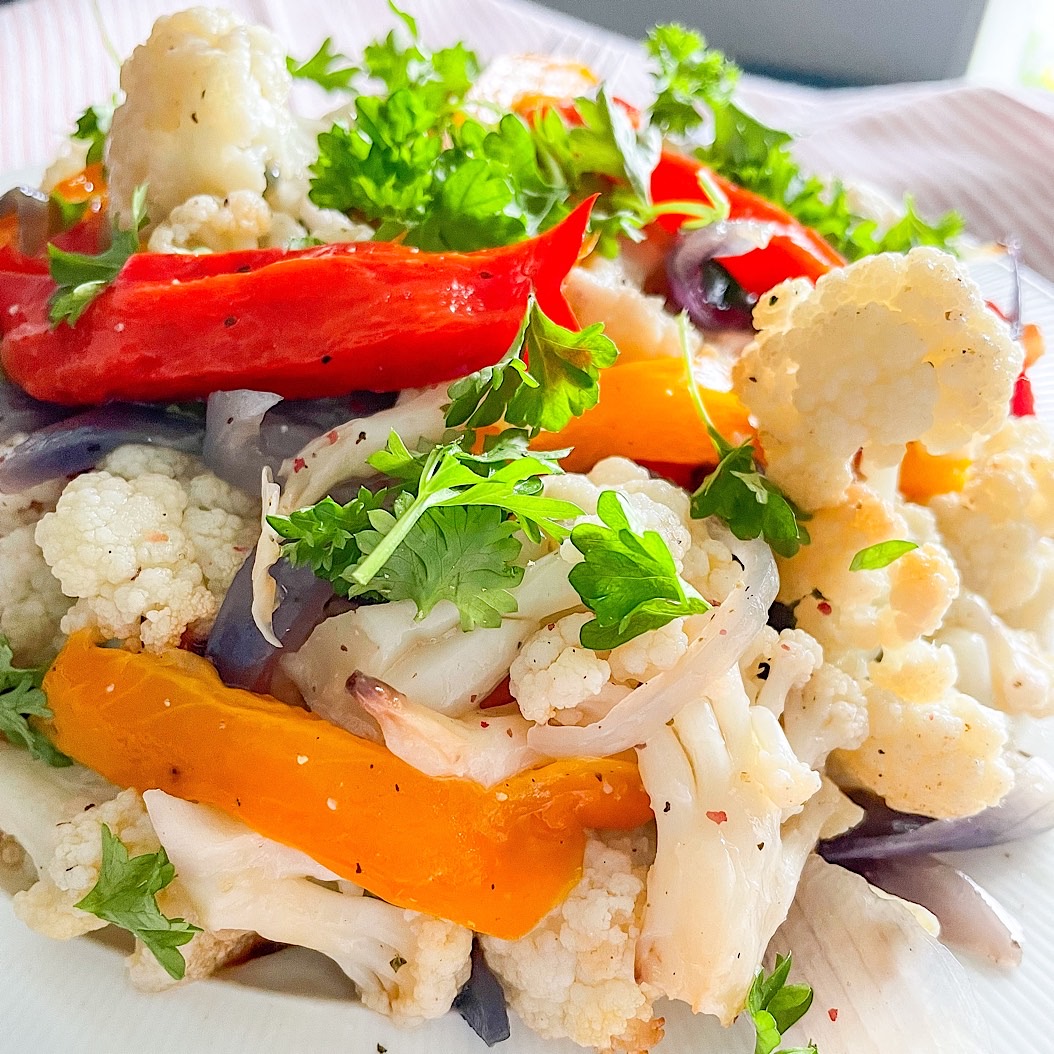 Close-up of warm roasted cauliflower salad with golden florets and sweet peppers