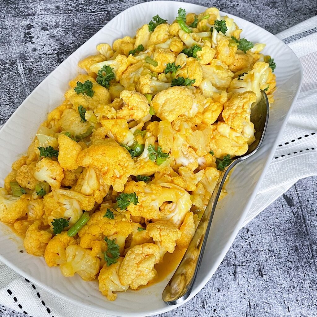 Cauliflower in coconut milk served on a white dish with spoon and fresh herbs
