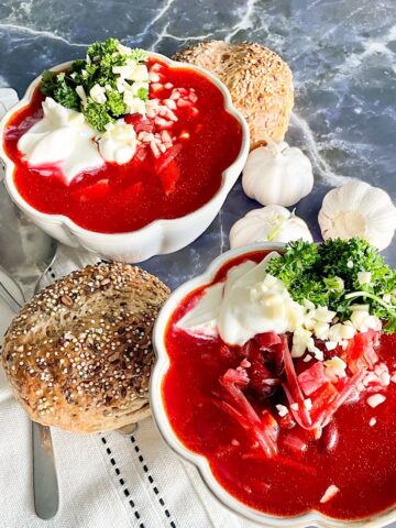 Two bowls of hearty beetroot soup with kidney beans, sour cream, parsley and seeded bread rolls