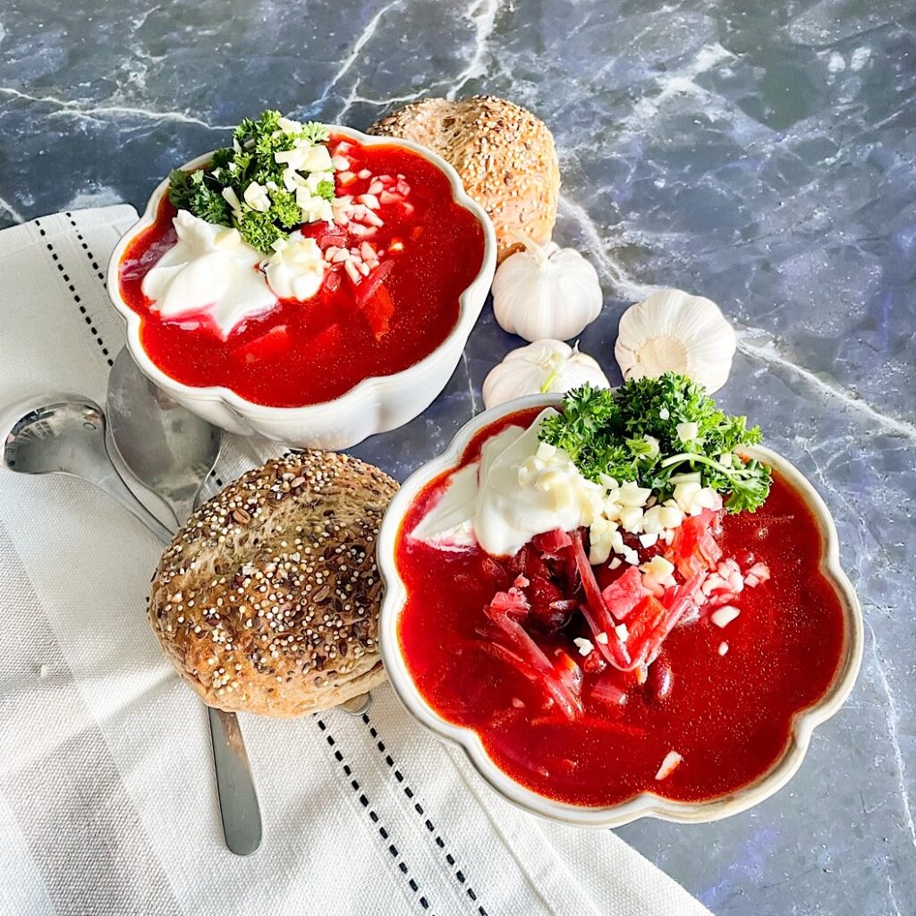 Healthy beetroot soup with kidney beans, sour cream and parsley beside seeded bread and garlic