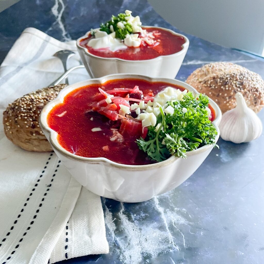  Homemade beetroot soup with kidney beans topped with sour cream, parsley and garlic in white bowls