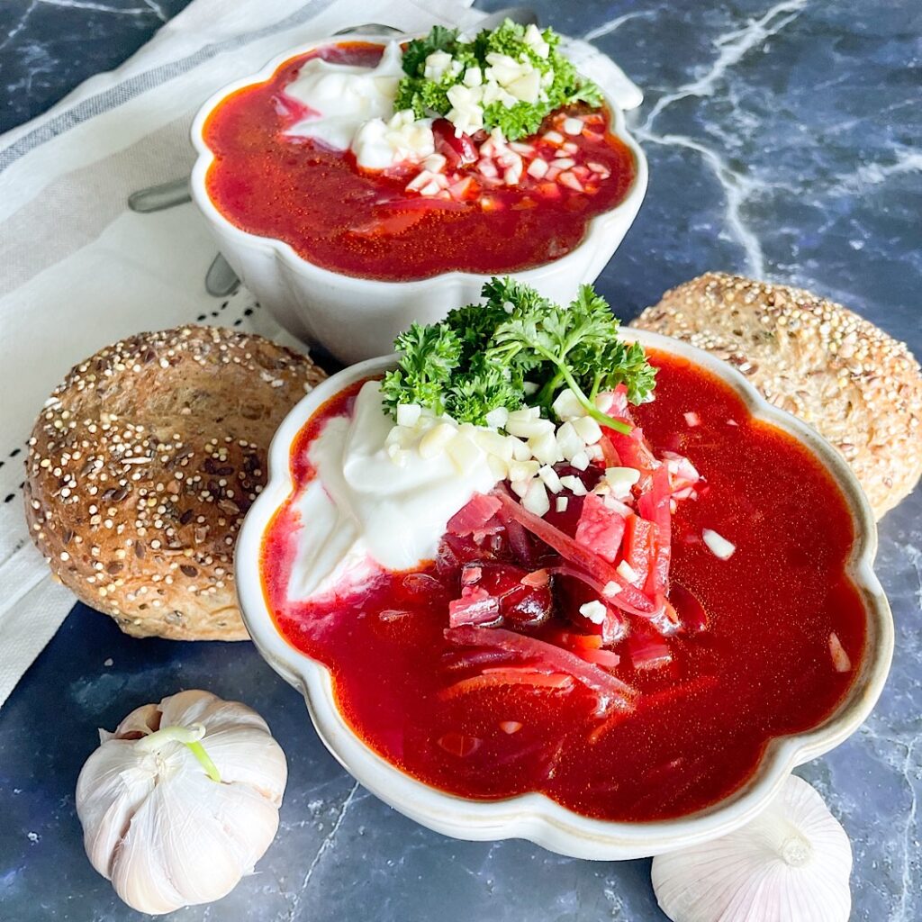 Vegetarian beetroot soup served in a white bowl with parsley, garlic and a seeded bread roll