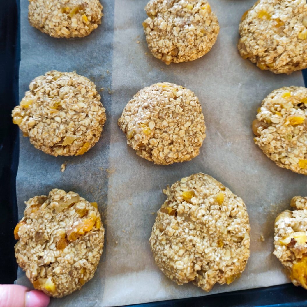 Apricot oatmeal cookie dough balls pressed down on a lined baking tray