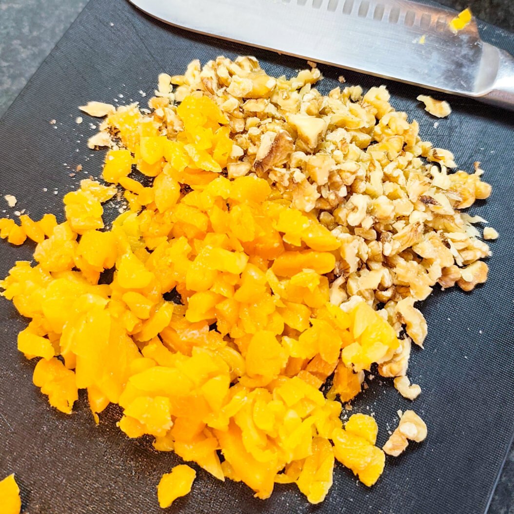 Chopped dried apricots and walnuts on a board for apricot oatmeal cookies