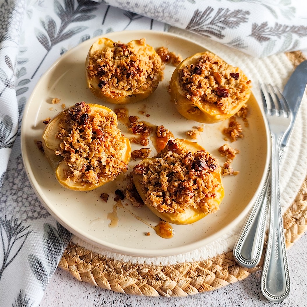 Halved baked apples topped with oat and pecan crumble on a beige ceramic plate. Perfect fall dessert idea.