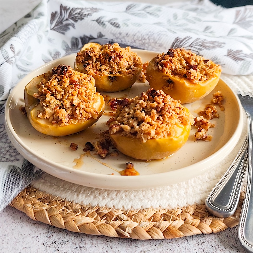Halved baked apples topped with oat and pecan crumble on a beige ceramic plate. Perfect fall dessert idea.