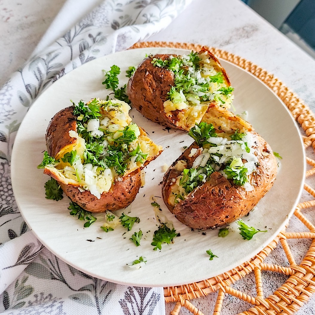 Plate of baked potatoes with crispy skin and herb butter topping.