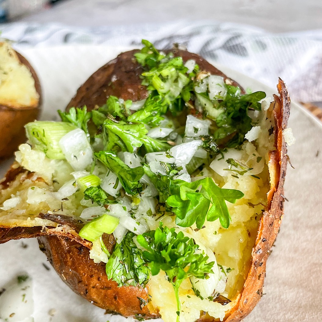 Close-up of crispy baked potato topped with fresh herbs and onions.