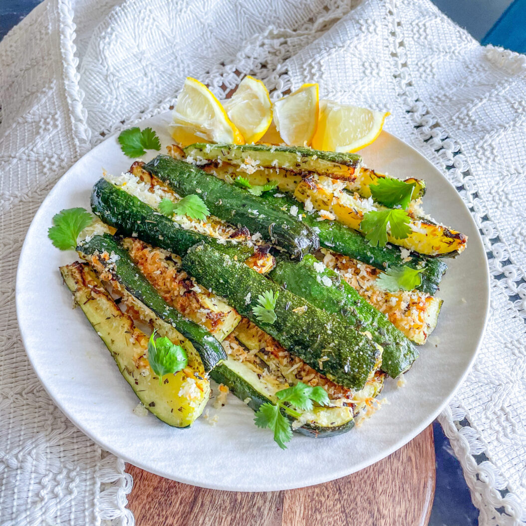Crispy parmesan roasted courgettes on a plate with lemon wedges and fresh coriander leaves