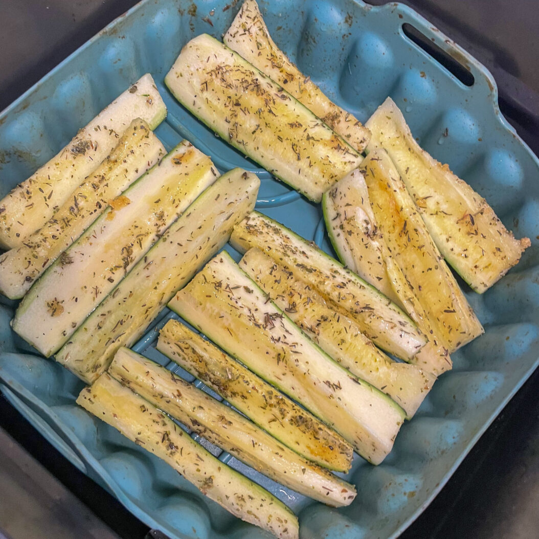 Seasoned courgette spears arranged skin-side down on blue tray before roasting
