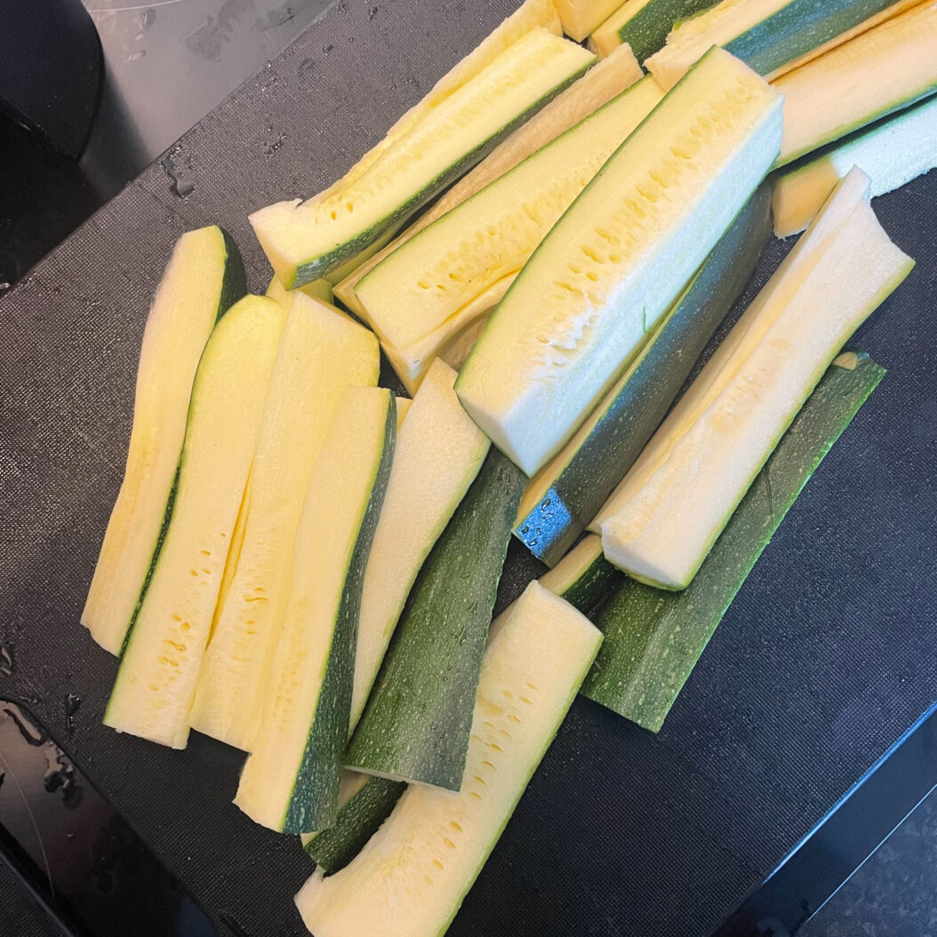 Sliced green and yellow courgette spears on chopping board ready for roasting