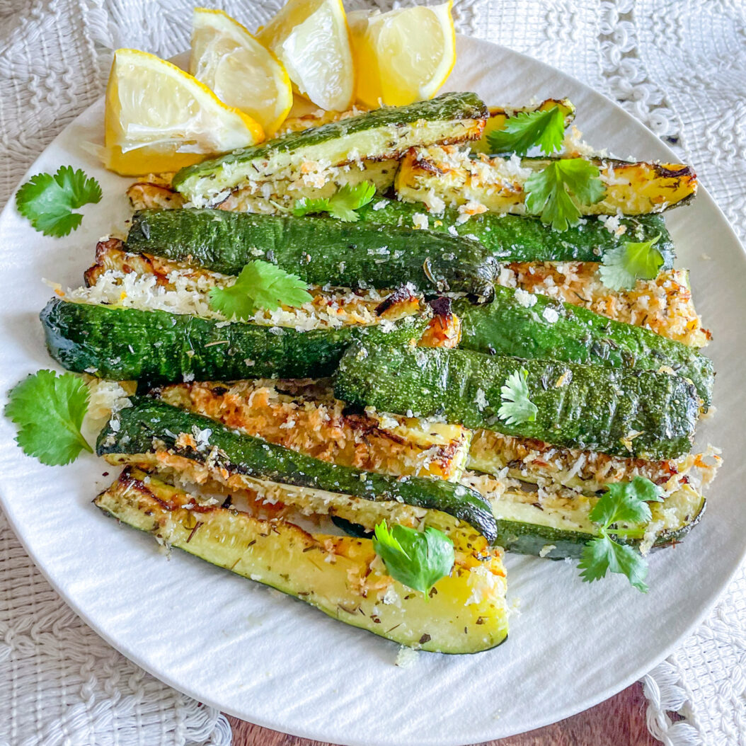 Easy roasted courgettes with parmesan crust and lemon wedges on a white plate