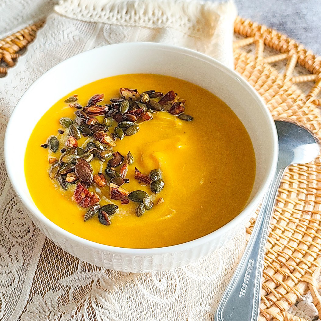 Creamy butternut squash soup with spicy seed topping in a white bowl on a woven placemat
