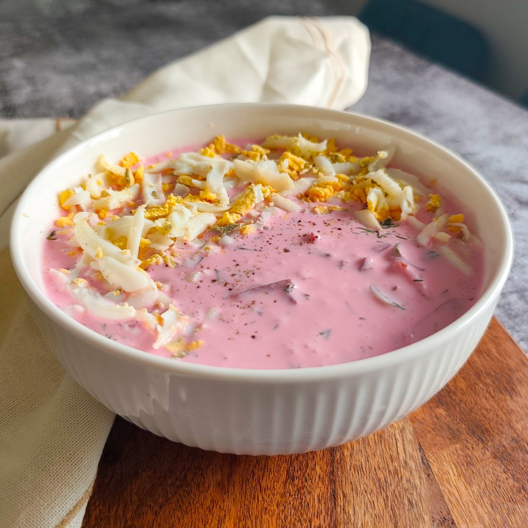 Traditional Šaltibarščiai Cold Borscht with eggs and dill, served in a ribbed bowl on wood board.