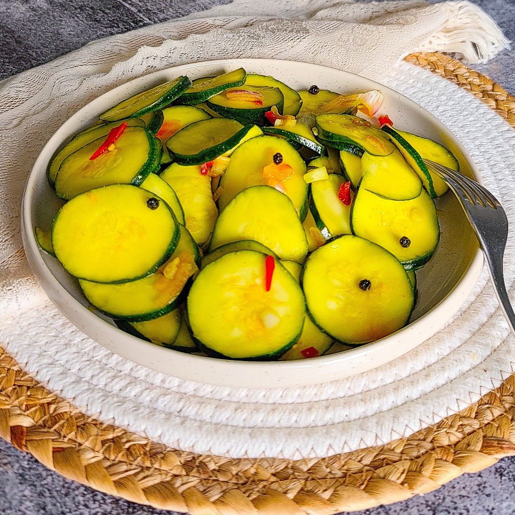 Thinly sliced pickled courgettes mixed with red chilli in a bright ceramic serving dish.