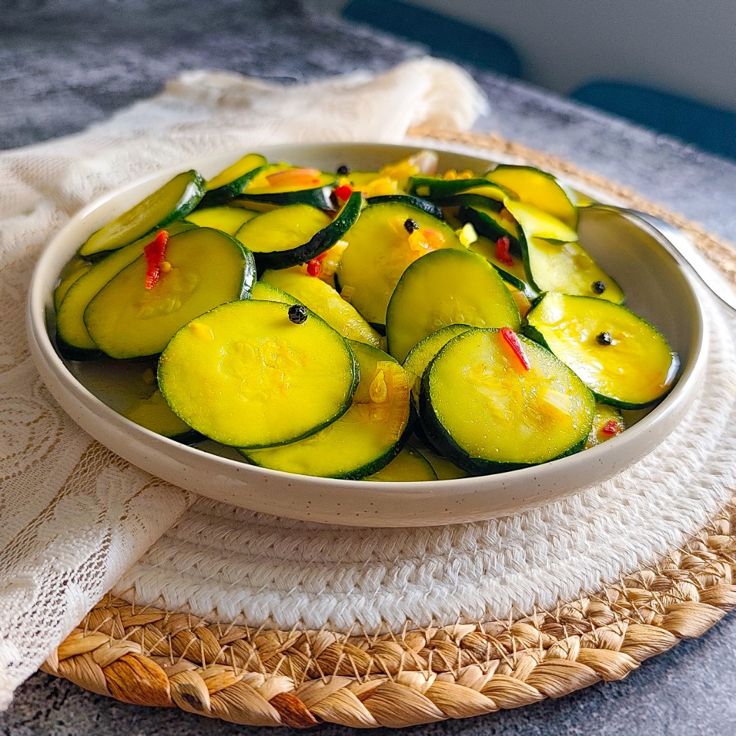 Close-up of crunchy pickled courgettes with sliced shallots and red chilli in golden marinade.