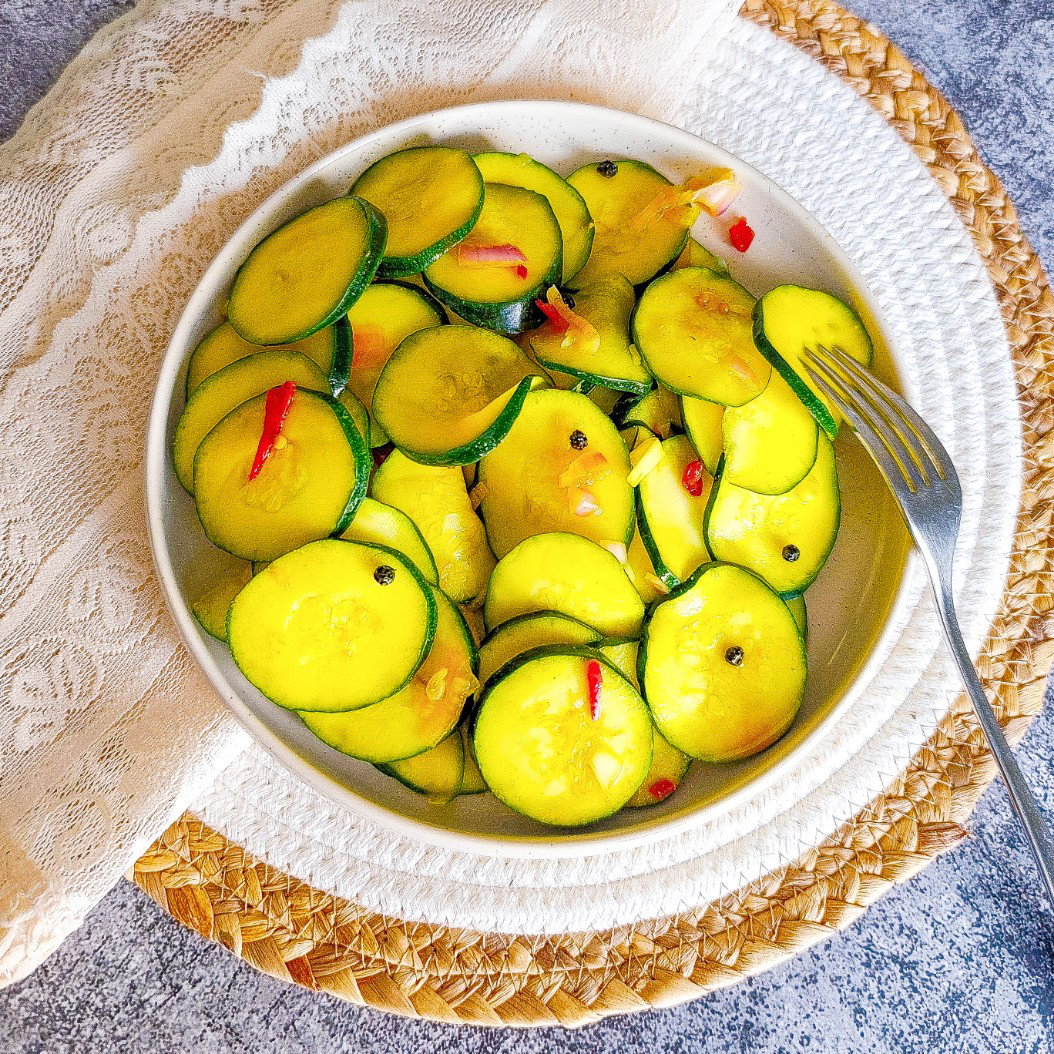 Homemade pickled courgettes served in a ceramic bowl with sliced chilli and turmeric brine.