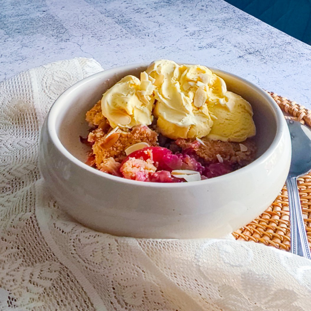 Side view of plum crumble with golden ice cream and almonds served in a ceramic bowl.