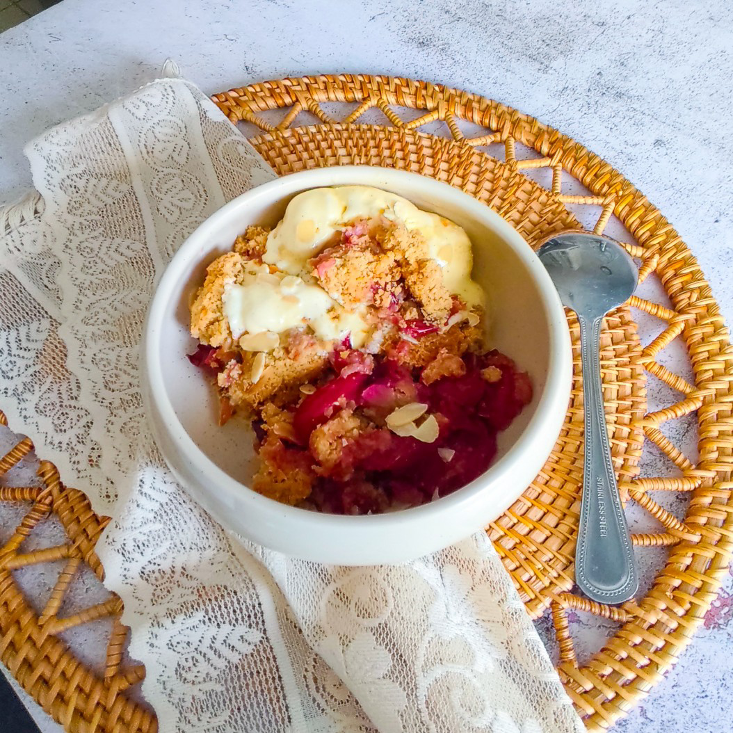 Golden plum crumble dessert with soft fruit filling and ice cream on a rustic placemat.