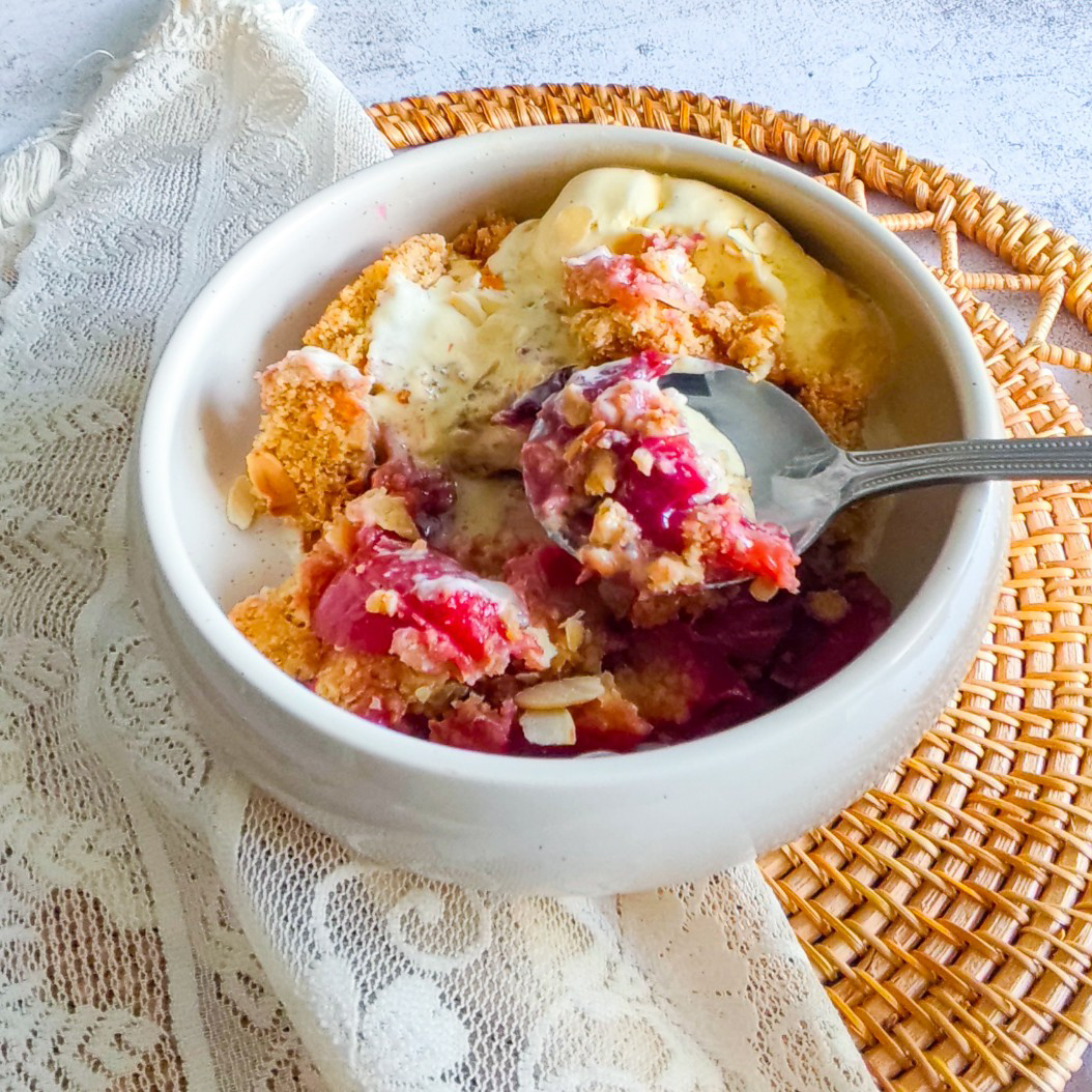 Close-up of plum crumble with melted ice cream and toasted almond flakes on top.