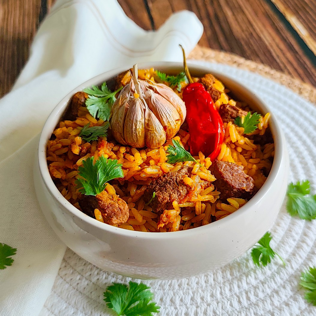 Plov with beef and turmeric rice, topped with whole garlic and red chilli