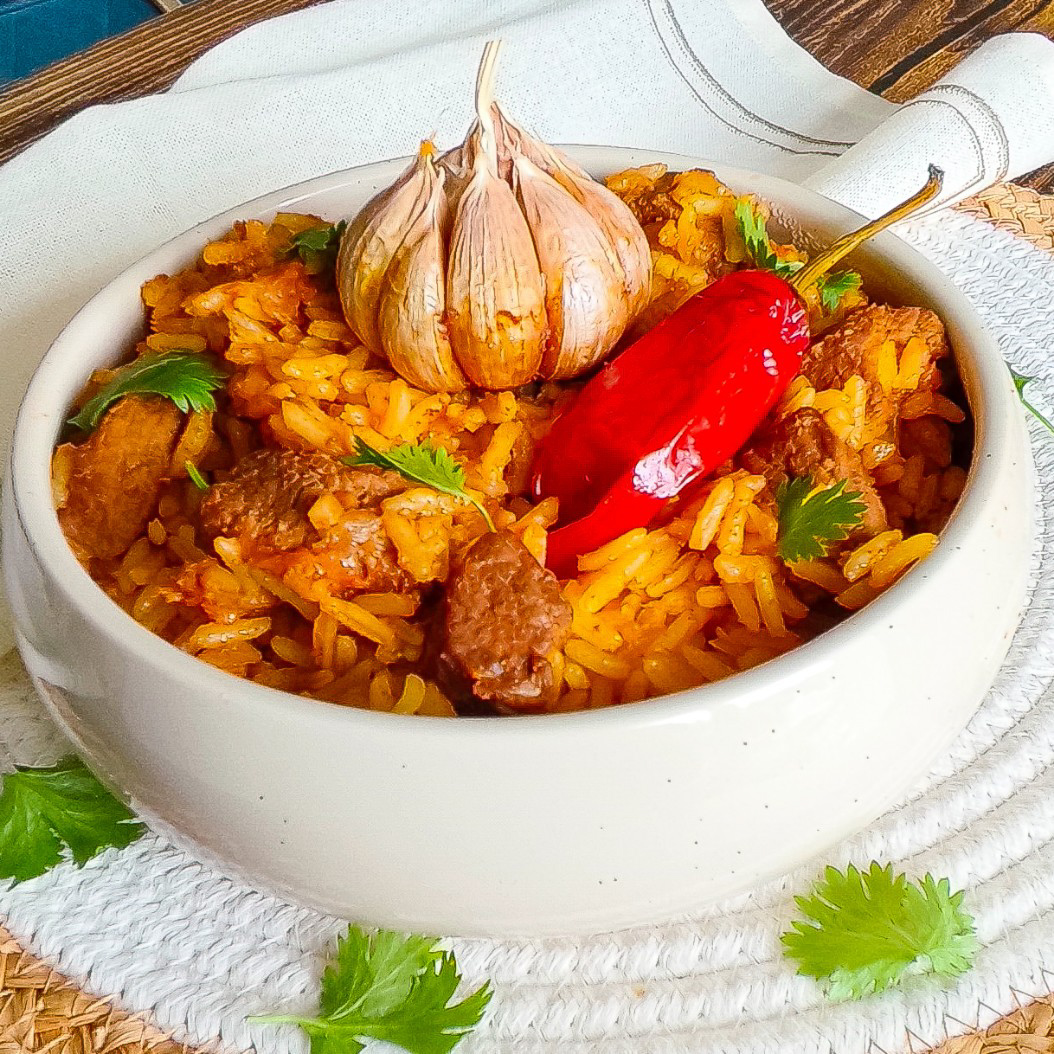 Traditional beef plov in a bowl with aromatic spices and coriander leaves