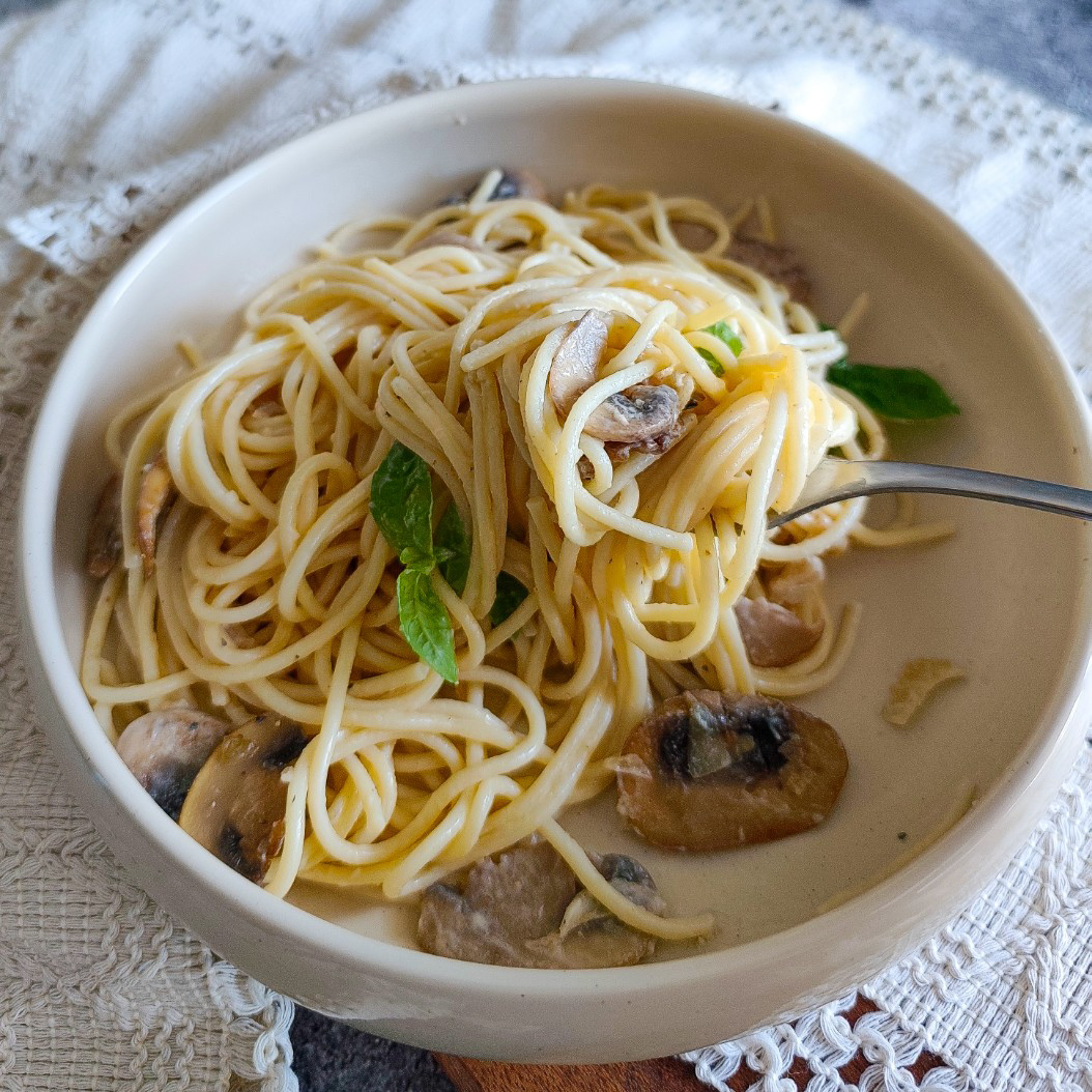 Fork twirling buttery mushroom pasta with basil leaves, served in a deep bowl with rich creamy sauce
