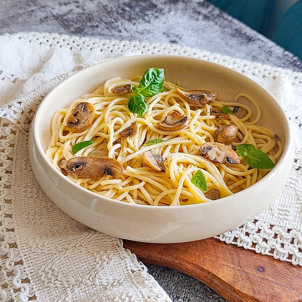Creamy garlic mushroom pasta in a white bowl with sautéed mushrooms and fresh herbs on rustic fabric
