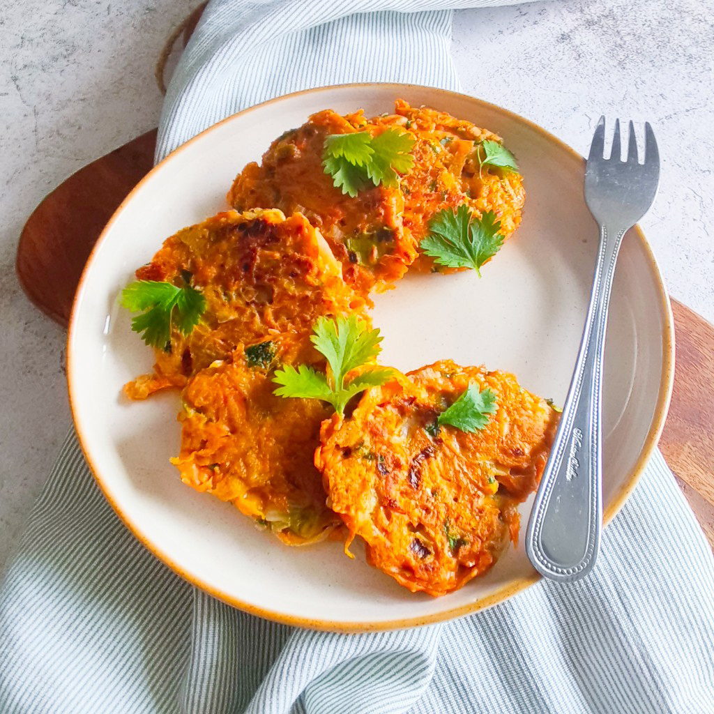 carrot fritters served on a ceramic plate with fresh coriander garnish, placed on a striped cloth with light background