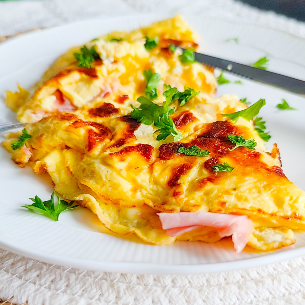 Ham and cheese omelette with a soft centre and melted cheese, garnished with parsley on a white plate.