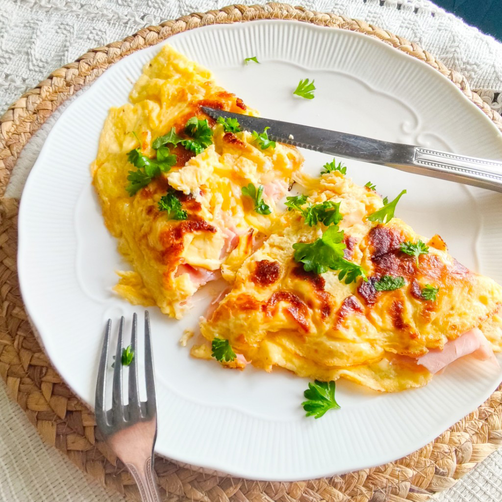 Ham and cheese omelette with golden top, cut open to reveal gooey cheese and ham, topped with fresh parsley.