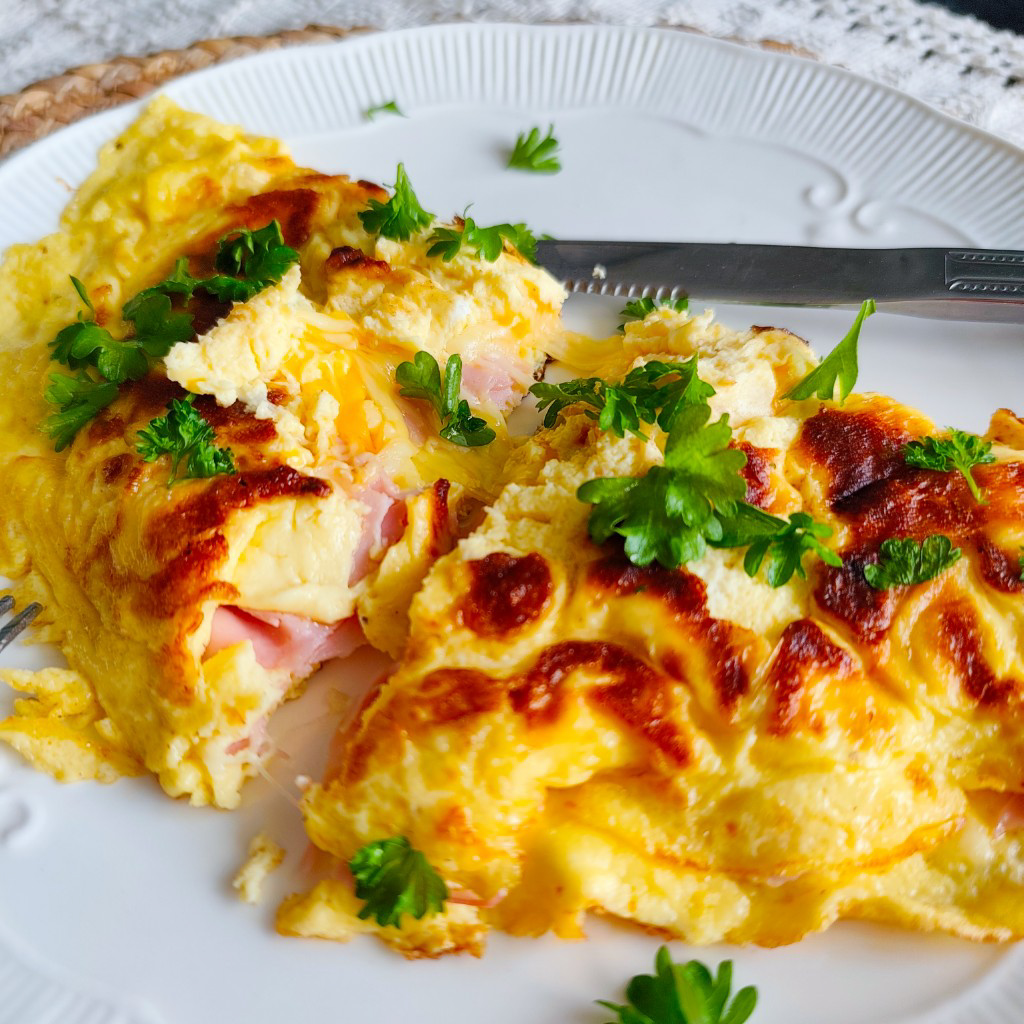Close-up of ham and cheese omelette garnished with parsley, sliced open to show melted cheese inside.