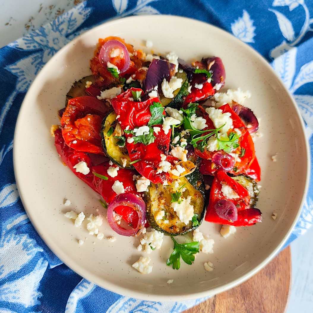 Bright, healthy roasted summer vegetables with feta cheese on a blue and white patterned cloth.