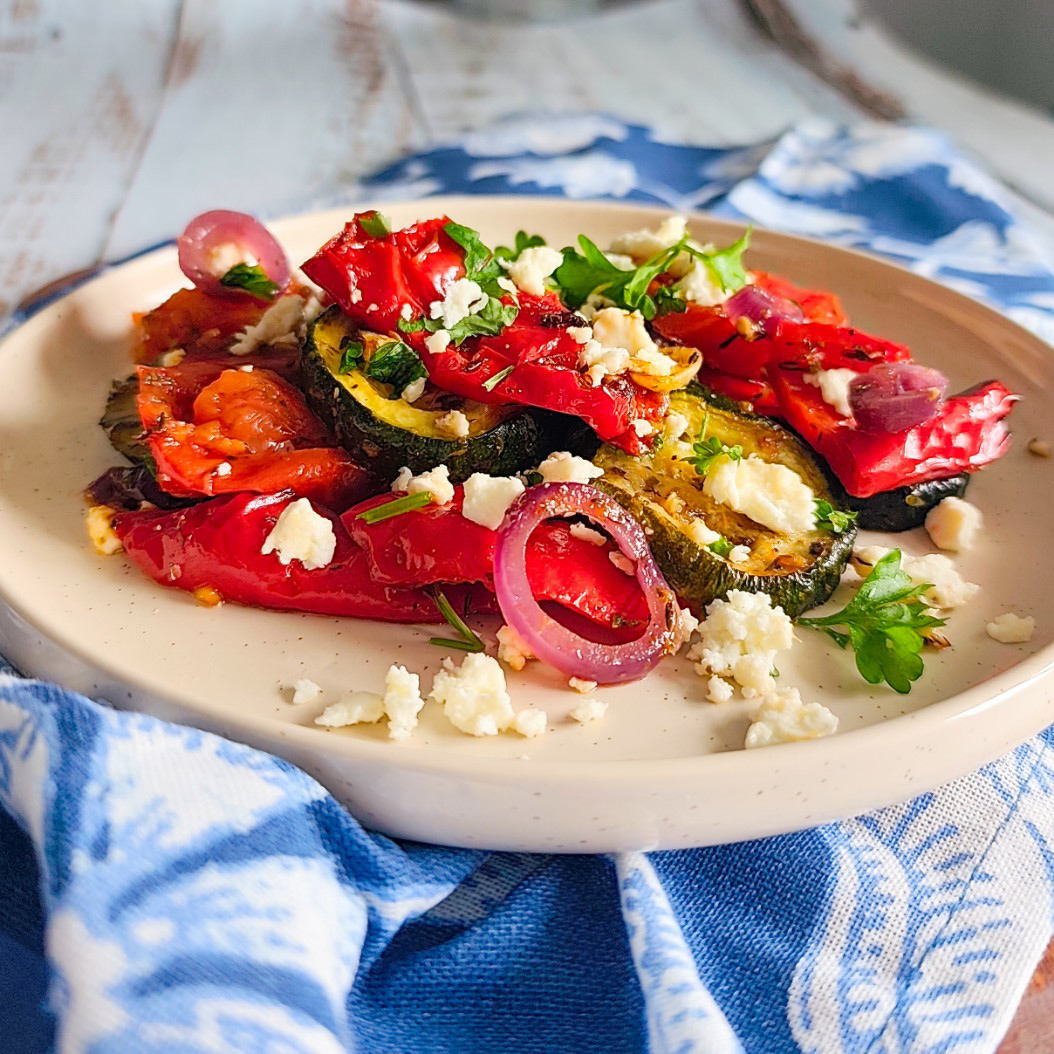 Colourful roasted summer vegetables garnished with parsley and crumbled feta